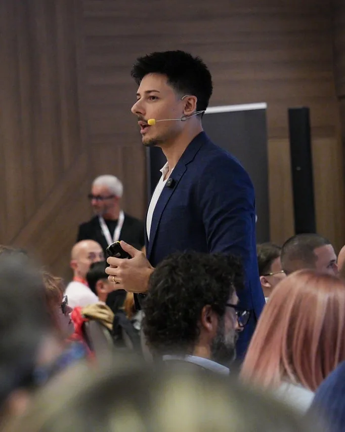 Angelo parla in sala, in piedi in mezzo al pubblico