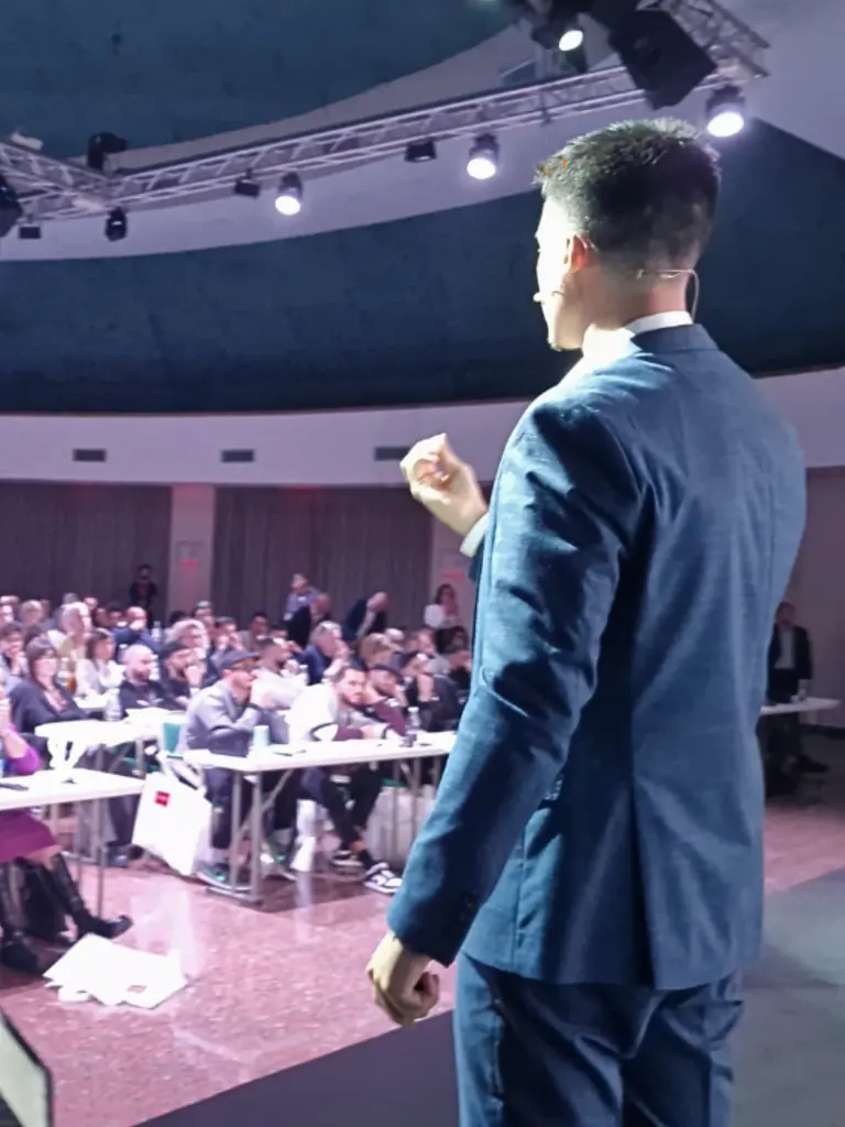 Angelo di spalle sul palco, davanti a una sala piena